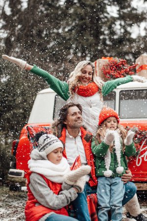 Téléchargez les photos : Bonne famille célébrant Noël et Nouvel An saison des vacances d'hiver en plein air. Enfants actifs avec des parents joyeux passer du temps ensemble embrasser s'amuser près de bus de Noël se réjouit à la première neige - en image libre de droit