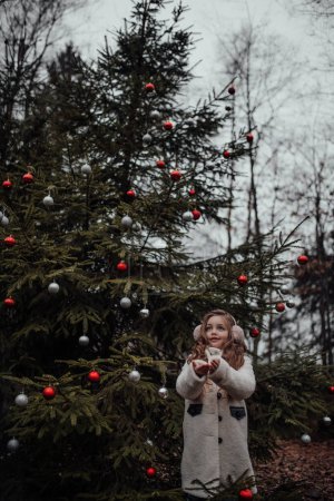 Photo for Female child celebrating Christmas and New Year winter holidays season outdoor. Active little girl joyful spending time at coniferous forest enjoying childhood - Royalty Free Image