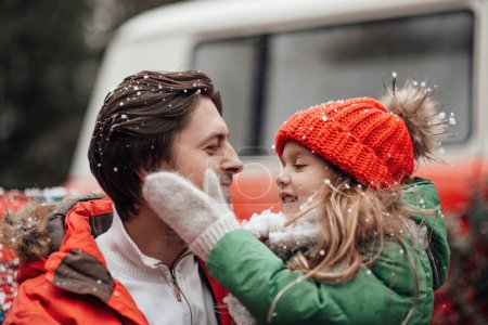Téléchargez les photos : Bonne famille célébrant Noël et Nouvel An saison des vacances d'hiver en plein air. Père avec petite fille joyeuse passer du temps ensemble embrasser s'amuser près de bus de Noël se réjouit à la première neige - en image libre de droit
