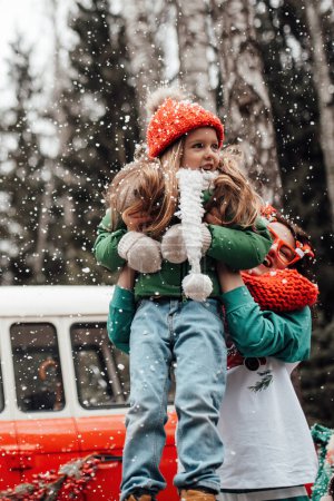 Téléchargez les photos : Enfants féminins célébrant Noël et Nouvel An saison des vacances d'hiver en plein air. Enfants actifs joyeux passer du temps ensemble s'amuser près de Noël bus se réjouit à la première neige profiter de l'enfance - en image libre de droit