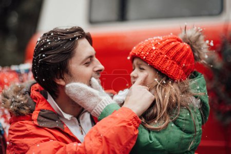 Foto de Feliz familia celebrando Navidad y Año Nuevo vacaciones de invierno temporada al aire libre. Padre con la pequeña hija alegre pasar tiempo juntos abrazos divertirse cerca de autobús de Navidad se regocija en la primera nieve - Imagen libre de derechos