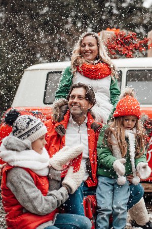 Photo for Happy family celebrating Christmas and New Year winter holidays season outdoor. Active kids with parents joyful spending time together hugging having fun near Xmas bus rejoices at first snow - Royalty Free Image