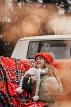 Téléchargez les photos : Enfant féminin célébrant Noël et Nouvel An saison des vacances d'hiver en plein air. Petite fille active en bonnet tricoté rouge joyeuse passer du temps en plein air avec canne à bonbons de Noël dans les mains - en image libre de droit