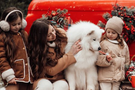 Foto de Feliz familia celebrando Navidad y Año Nuevo vacaciones de invierno temporada al aire libre. Niños con madre y perros blancos Samoyedo alegre pasar tiempo juntos abrazos cerca de Navidad viejo autobús - Imagen libre de derechos