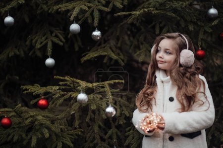 Foto de Niña activa descansar en el bosque disfrutando de la infancia decorando bolas árbol de Navidad. Niña celebrando Navidad y Año Nuevo vacaciones de invierno temporada al aire libre - Imagen libre de derechos