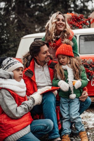 Téléchargez les photos : Bonne famille célébrant Noël et Nouvel An saison des vacances d'hiver en plein air. Enfants actifs avec des parents joyeux passer du temps ensemble embrasser s'amuser près de bus de Noël se réjouit à la première neige - en image libre de droit