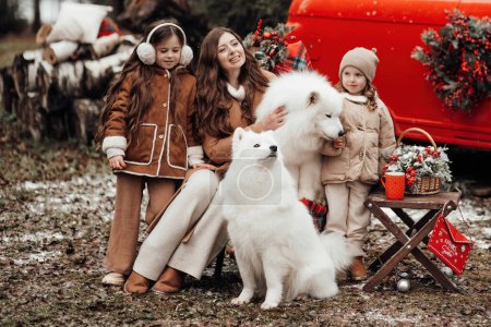 Téléchargez les photos : Bonne famille célébrant Noël et Nouvel An saison des vacances d'hiver en plein air. Enfants avec mère et blanc Samoyed chiens joyeux passer du temps ensemble étreignant près de Noël vieux bus - en image libre de droit