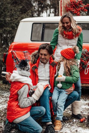 Photo for Happy family celebrating Christmas and New Year winter holidays season outdoor. Active kids with parents joyful spending time together hugging having fun near Xmas bus rejoices at first snow - Royalty Free Image