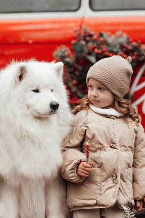 Foto de Niña celebrando Navidad y Año Nuevo vacaciones de invierno temporada al aire libre. Niño con los perros Samoyedo blanco alegre pasar tiempo juntos cerca de Navidad viejo autobús - Imagen libre de derechos