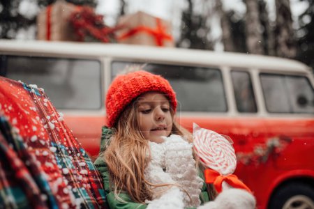 Photo for Female child celebrating Christmas and New Year winter holidays season outdoor. Active little girl in red knitted hat joyful spending time on open air with Xmas candy cane in hands - Royalty Free Image