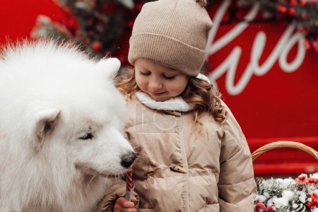 Foto de Niña celebrando Navidad y Año Nuevo vacaciones de invierno temporada al aire libre. Niño con los perros Samoyedo blanco alegre pasar tiempo juntos cerca de Navidad viejo autobús - Imagen libre de derechos