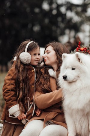 Foto de Feliz familia celebrando Navidad y Año Nuevo vacaciones de invierno temporada al aire libre. Hija con la madre y el perro blanco Samoyed alegre pasar tiempo juntos abrazos cerca de Navidad viejo autobús - Imagen libre de derechos