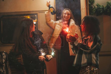 Foto de Chicas felices celebrando Navidad y Año Nuevo vacaciones de invierno temporada al aire libre. Jóvenes activos diversas mujeres alegres amigas junto con las luces de Bengala chispas se divierten cerca del viejo tráiler de Navidad - Imagen libre de derechos