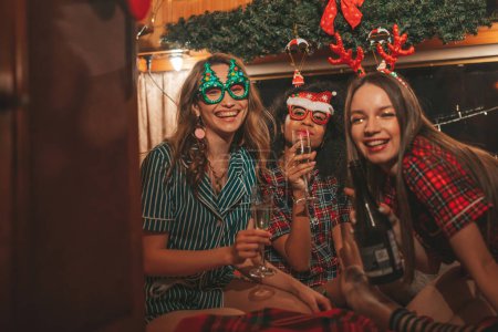 Photo for Happy girls celebrating Christmas and New Year winter holidays season in camper. Active young diverse women joyful spending time together hugging have fun drinking sparkling wine in old xmas trailer - Royalty Free Image
