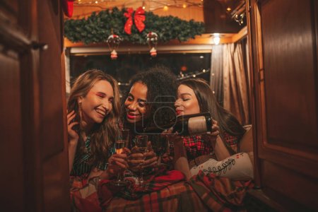 Photo for Happy girls celebrating Christmas and New Year winter holidays season in camper. Active young diverse women joyful spending time together hugging have fun drinking sparkling wine in old xmas trailer - Royalty Free Image