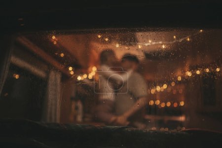 Photo for Happy couple celebrating Christmas and New Year winter holidays season in Camper Park. Young couple rest spending time together hugs and kisses in window of Xmas camper trailer - Royalty Free Image