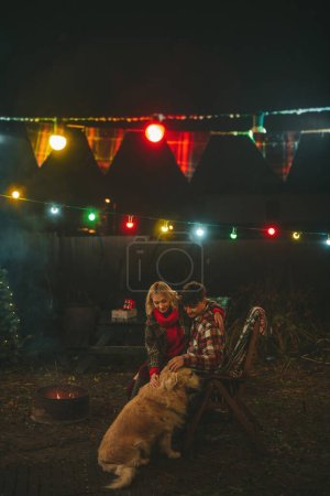 Foto de Pareja feliz celebrando Navidad y Año Nuevo temporada de vacaciones de invierno en Camper Park. Joven pareja alegre abrazo y pasar tiempo juntos con perro golden retriever cerca de la caravana de Navidad remolque - Imagen libre de derechos