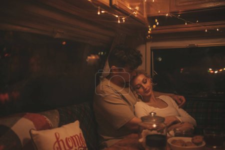 Photo for Happy couple celebrating Christmas and New Year winter holidays season in camper. Young couple drinking tea spending time together hugs and kisses in Xmas camper trailer - Royalty Free Image