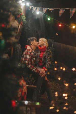 Glückliches Paar, das Weihnachten und Neujahr im Camper Park feiert. Junges Paar verbringt Zeit mit Umarmungen und Küssen in der Nähe des Wohnmobilanhängers zu Weihnachten