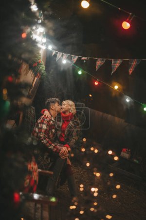 Photo for Happy couple celebrating Christmas and New Year winter holidays season in Camper Park. Young couple rest and relaxation spending time together hugs and kisses near Xmas camper trailer - Royalty Free Image