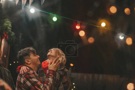 Téléchargez les photos : Joyeux couple célébrant Noël et Nouvel An saison des vacances d'hiver dans Camper Park. Jeune couple de repos et de détente passer du temps ensemble câlins et baisers près de caravane camping-car de Noël - en image libre de droit