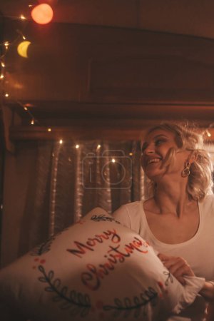 Photo for Happy young woman celebrating Christmas and New Year winter holidays season in camper. Young woman having fun pillow fight in Xmas camper trailer - Royalty Free Image