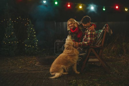 Photo for Happy couple celebrating Christmas and New Year winter holidays season in Camper Park. Young joyful couple hugging and spending time together with golden retriever dog near Xmas camper trailer - Royalty Free Image