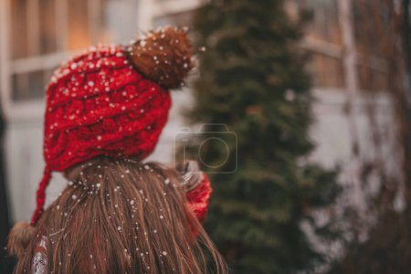 Photo for Back view of little girl celebrating Christmas and New Year winter holidays season outdoor, waiting Santa near Xmas camper trailer and rejoices at first snow enjoying childhood - Royalty Free Image