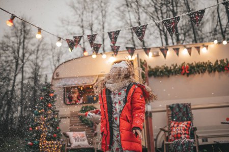 Téléchargez les photos : Petite fille célébrant Noël et Nouvel An saison des vacances d'hiver en plein air, attendant Santa près de caravane camping-car de Noël et se réjouit à la première neige profiter de l'enfance - en image libre de droit