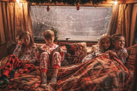 Téléchargez les photos : Enfants célébrant Noël et Nouvel An saison des vacances d'hiver en camping-car. Les enfants actifs passent du temps ensemble grimace avoir du plaisir et lire le livre à Noël caravane camping-car profiter de l'enfance - en image libre de droit