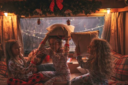 Photo for Female children celebrating Christmas and New Year winter holidays season in camper. Active kids joyful spending time together having fun pillow fight in Xmas camper trailer enjoying childhood - Royalty Free Image