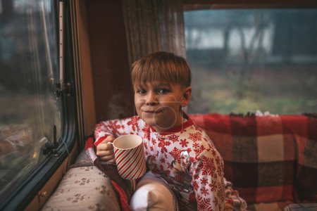 Photo for Little boy drinks milk while celebrating Christmas and New Year winter holidays season and waiting Santa at Xmas camper trailer - Royalty Free Image