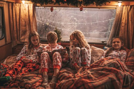 Photo for Children celebrating Christmas and New Year winter holidays season in camper. Active kids spending time together grimace having fun and reading book at Xmas camper trailer enjoying childhood - Royalty Free Image