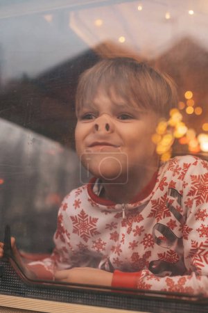 Téléchargez les photos : Petit garçon faire des visages tout en célébrant Noël et Nouvel An saison des vacances d'hiver attendant Père Noël au camping-car de Noël remorque - en image libre de droit