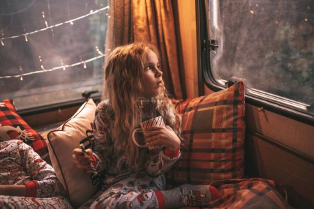 Photo for Little girl drinks milk while celebrating Christmas and New Year winter holidays season and waiting Santa at Xmas camper trailer - Royalty Free Image