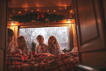 Photo for Children celebrating Christmas and New Year winter holidays season in camper. Active kids spending time together grimace having fun and reading book at Xmas camper trailer enjoying childhood - Royalty Free Image