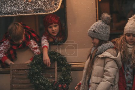 Foto de Los niños que celebran la Navidad y Año Nuevo vacaciones de invierno temporada al aire libre esperando a Santa. Niños alegre pasar tiempo juntos cerca de Navidad caravana remolque se regocija en la primera nieve disfrutando de la infancia - Imagen libre de derechos