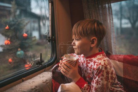 Téléchargez les photos : Petit garçon boit du lait tout en célébrant Noël et le Nouvel An saison des vacances d'hiver et d'attendre le Père Noël au camping-car de Noël remorque - en image libre de droit