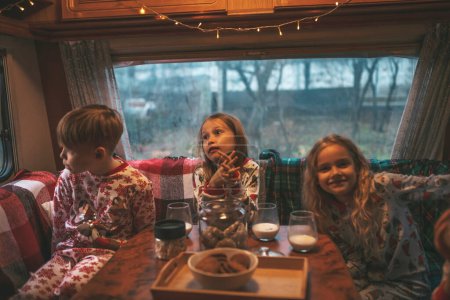 Foto de Niños celebrando Navidad y Año Nuevo temporada de vacaciones de invierno esperando a Santa Claus en autocaravana. Los niños que pasan tiempo juntos tomando algo de leche disfrutan del bastón de caramelo y las galletas en el remolque de la caravana de Navidad - Imagen libre de derechos