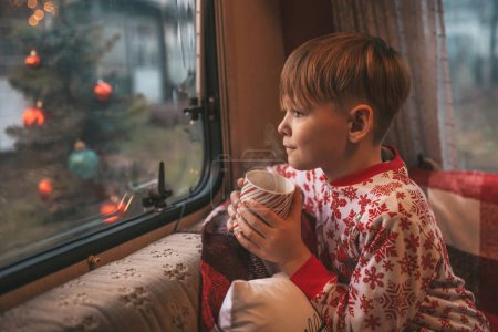 Téléchargez les photos : Petit garçon boit du lait tout en célébrant Noël et le Nouvel An saison des vacances d'hiver et d'attendre le Père Noël au camping-car de Noël remorque - en image libre de droit