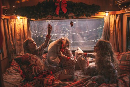 Téléchargez les photos : Enfants femmes célébrant Noël et Nouvel An saison des vacances d'hiver en camping-car. Enfants actifs joyeux passer du temps ensemble avoir bataille d'oreillers amusant dans caravane de camping-car de Noël profiter de l'enfance - en image libre de droit