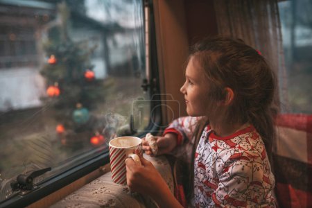 Photo for Little girl drinks milk while celebrating Christmas and New Year winter holidays season and waiting Santa at Xmas camper trailer - Royalty Free Image
