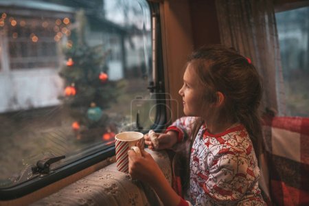 Téléchargez les photos : Petite fille boit du lait tout en célébrant Noël et Nouvel An saison des vacances d'hiver et en attendant le Père Noël au camping-car de Noël remorque - en image libre de droit