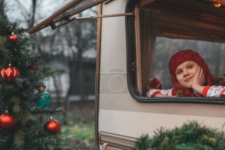 Téléchargez les photos : Petite fille célébrant Noël et Nouvel An saison des vacances d'hiver et attendant le Père Noël au camping-car de Noël remorque - en image libre de droit