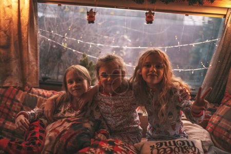 Téléchargez les photos : Enfants célébrant Noël et Nouvel An saison des vacances d'hiver en camping-car. Petites filles joyeuses passer du temps ensemble grimace chuchotant secrets dans l'oreille à caravane de camping-car de Noël profiter de l'enfance - en image libre de droit