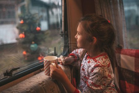 Téléchargez les photos : Petite fille boit du lait tout en célébrant Noël et Nouvel An saison des vacances d'hiver et en attendant le Père Noël au camping-car de Noël remorque - en image libre de droit