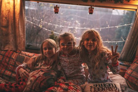 Photo for Children celebrating Christmas and New Year winter holidays season in camper. Little girls joyful spending time together grimace whispering secrets in ear at Xmas camper trailer enjoying childhood - Royalty Free Image