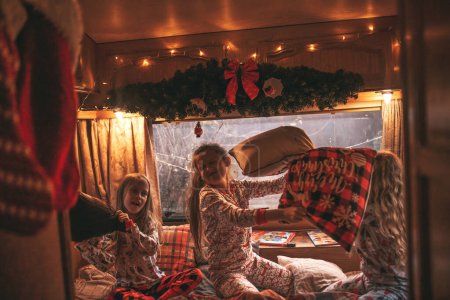 Photo for Female children celebrating Christmas and New Year winter holidays season in camper. Active kids joyful spending time together having fun pillow fight in Xmas camper trailer enjoying childhood - Royalty Free Image