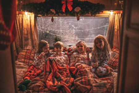 Téléchargez les photos : Les enfants qui célèbrent Noël et le Nouvel An saison des vacances d'hiver attendent le Père Noël en camping-car. Les enfants passant du temps ensemble grimace boire du lait profiter de la canne à bonbons et des biscuits à la caravane de Noël - en image libre de droit