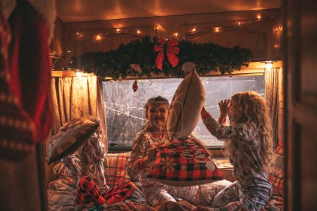 Téléchargez les photos : Enfants femmes célébrant Noël et Nouvel An saison des vacances d'hiver en camping-car. Enfants actifs joyeux passer du temps ensemble avoir bataille d'oreillers amusant dans caravane de camping-car de Noël profiter de l'enfance - en image libre de droit